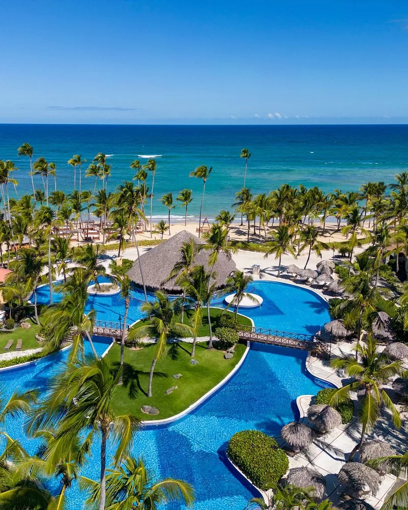 Palmeras y piscinas junto a la playa y el mar Caribe en Punta Cana